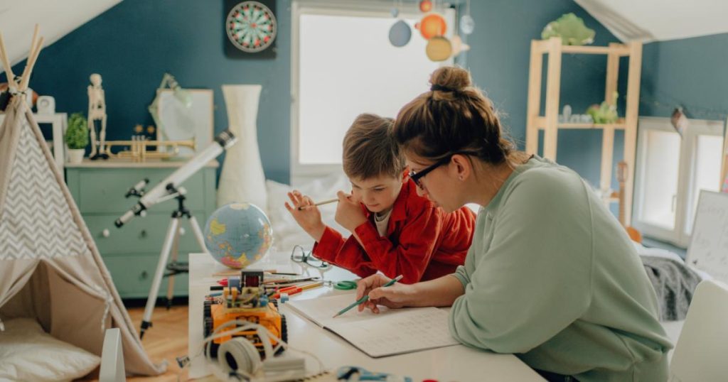 A Quick Guide to Montessori Homeschool. Image shows a parent helping a child with school assignment in the foreground. They are sitting at a desk writing in a notebook. In the background is the child's bedroom, painted in soft green and blue colors with a telescope and a globe.