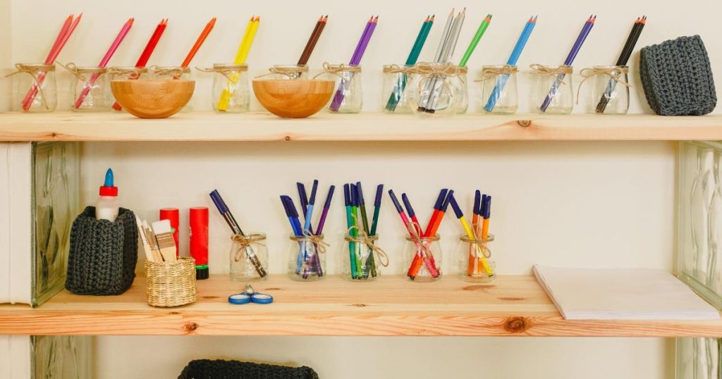 Beyond Early Childhood and Materials: Montessori Across the Planes of Development, an interview with Dr. Luz Casquejo Johnston. Image shows a shelf in a Montessori classroom. The top shelf has glass jars that contain colored pencils leaning to the right. This middle she has glue, scissors and markers.