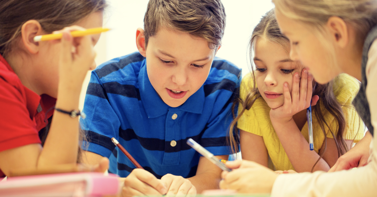 Executive Functioning Skills in the Montessori Elementary Classroom. Image shows four elementary aged students gathered at a table with pencils in their hands.